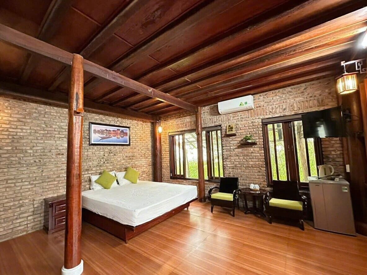 A room with a bed, wooden floor, brick walls, a window, and a small table with chairs.