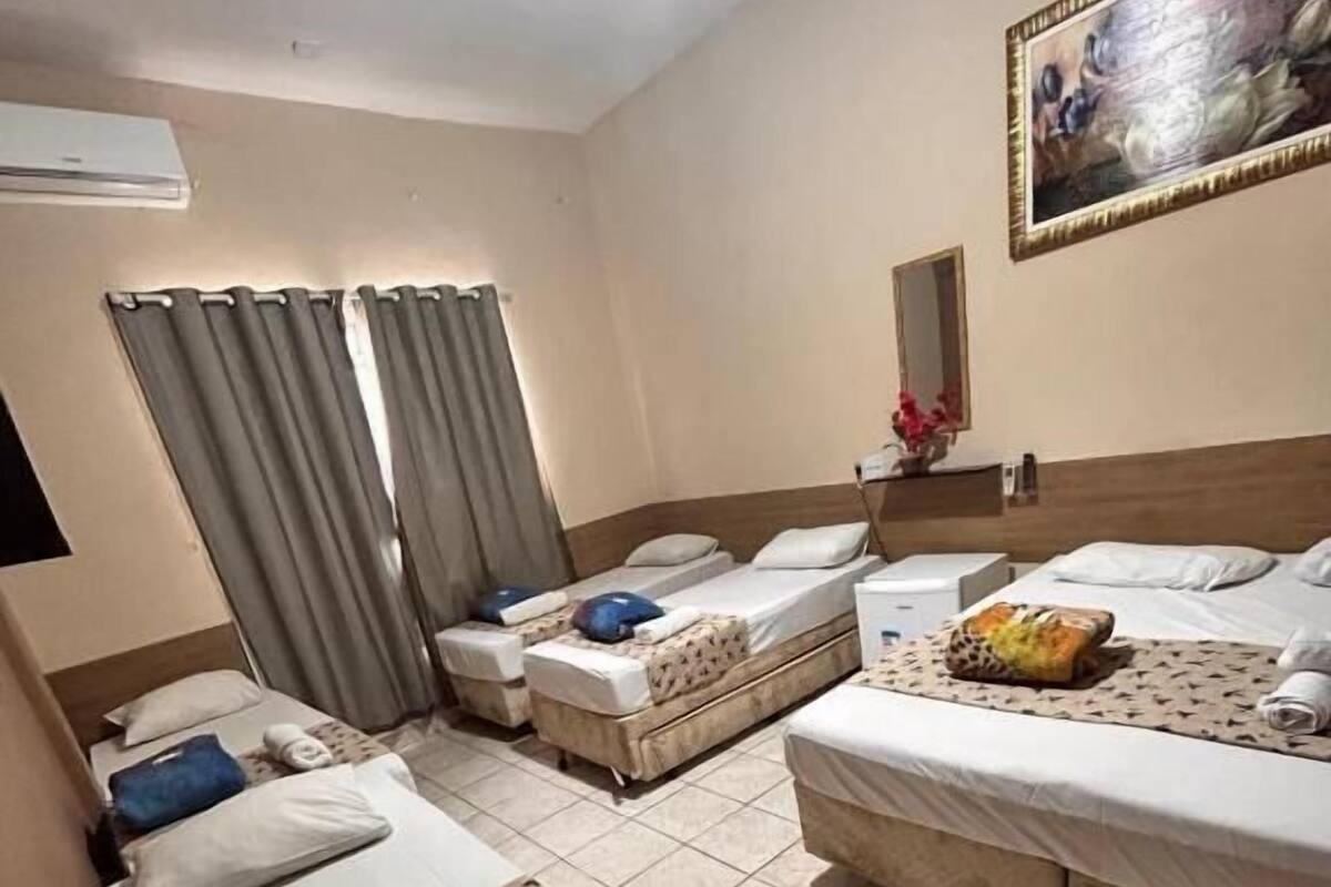 A hotel room with three beds, a painting on the wall, and an air conditioning unit.