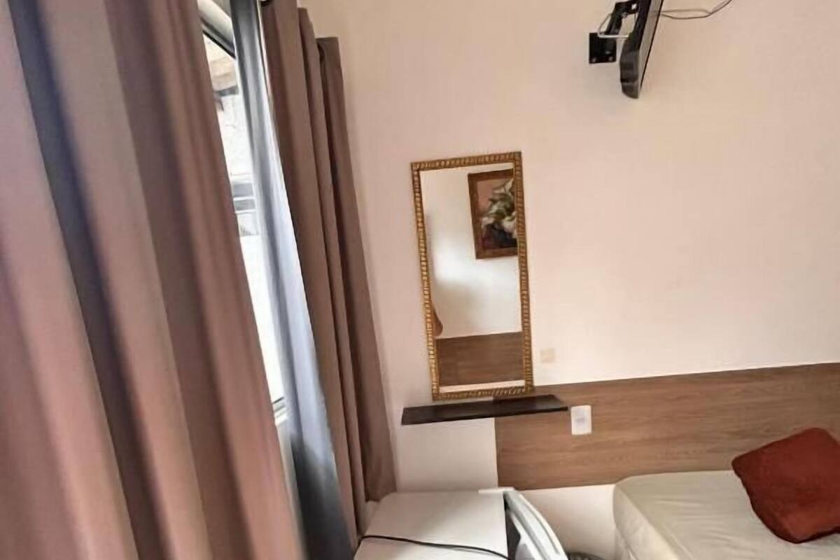 A hotel room with a bed, a desk, a chair, a TV, and a mirror.