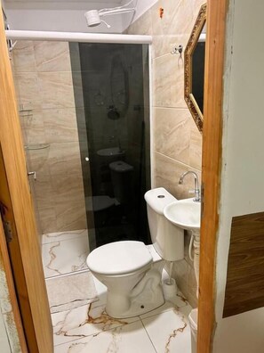 Un baño con cabina de ducha de vidrio, inodoro y lavamanos.