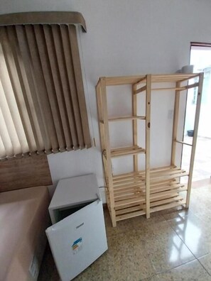 Una habitación con una estantería de madera, un refrigerador blanco y una ventana con persianas.