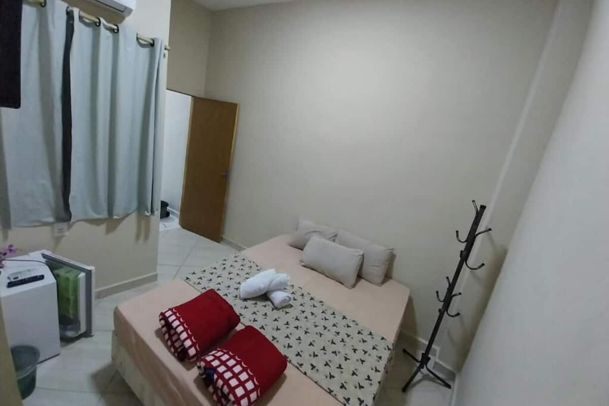 A small, tidy room with a bed, a coat rack, and a window.