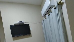 A small room with a TV mounted on the wall, a mini-fridge, a small table with a plant, and a red chair.