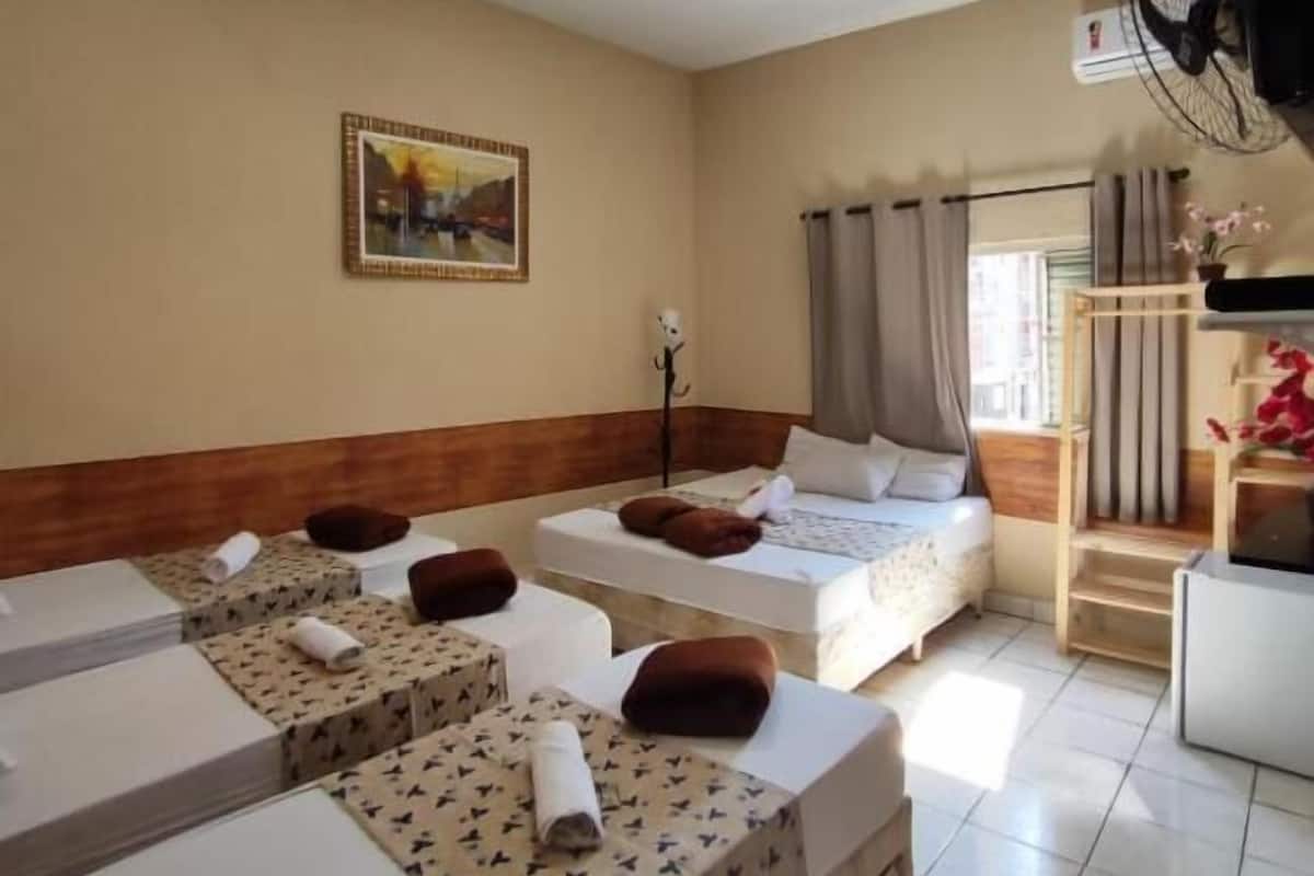 A hotel room with multiple beds, a television, a fan, and a window with curtains.