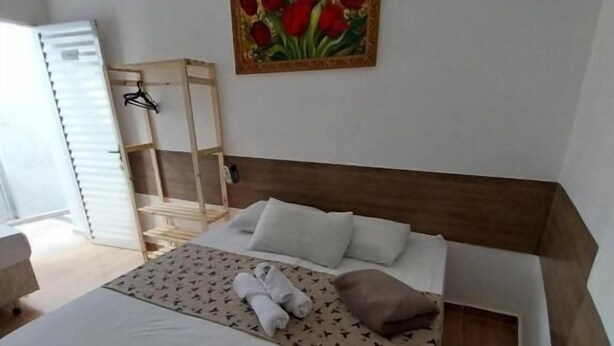 A bedroom with a bed, pillows, a painting, a wooden headboard, and a side table.