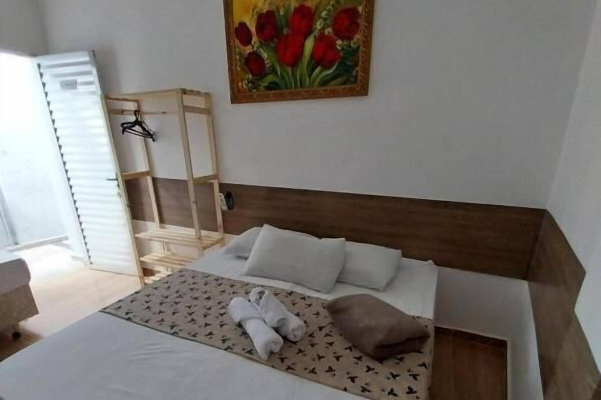 A bedroom with a bed, pillows, a painting, a wooden headboard, and a side table.