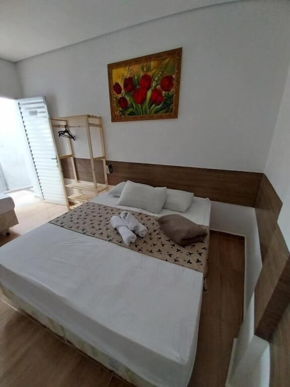 A bedroom with a bed, pillows, a painting, a wooden headboard, and a side table.
