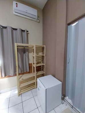 A room with a wooden wardrobe, a small white appliance, and a window with curtains.