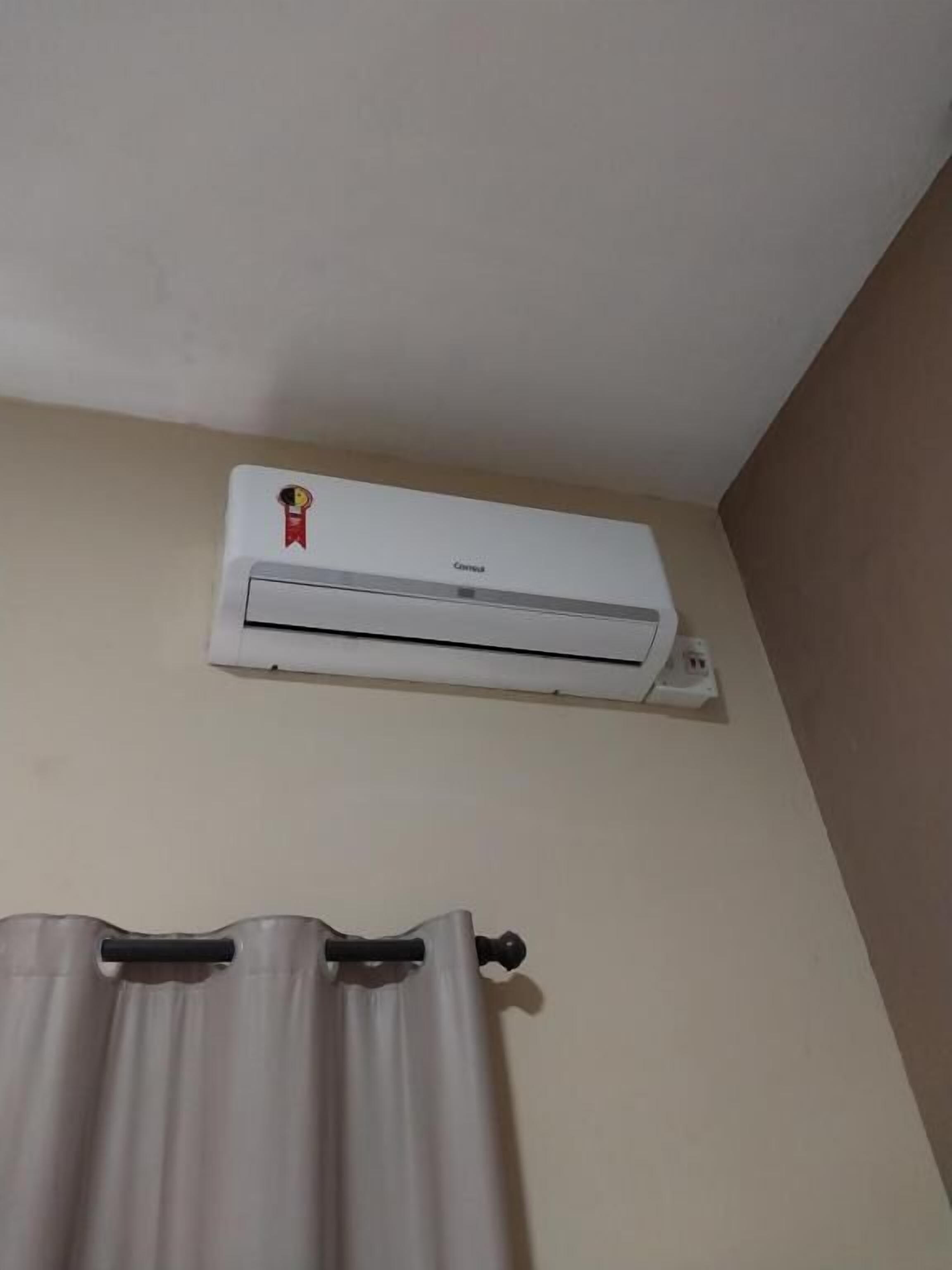 A white air conditioning unit mounted on a wall with a curtain rod below it.