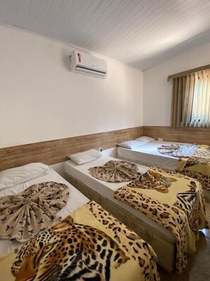 Habitación de hotel con varias camas, cada una con ropa de cama de estampado de leopardo. Cuenta con un ventilador de techo y un equipo de aire acondicionado.