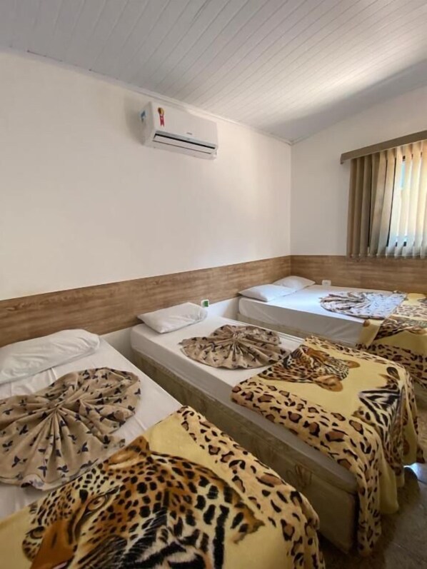 A hotel room with multiple beds, each with leopard-print bedding. There is a ceiling fan and an air conditioning unit.