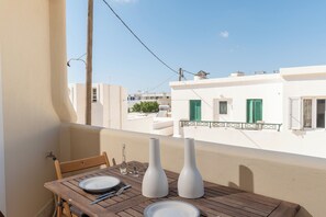 Ein Balkon mit Holztisch, gedecktem Esstisch, weißen Vasen und Blick auf Gebäude mit grünen Fensterläden.