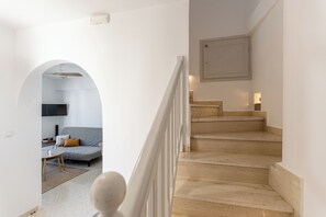 Eine Treppe führt zu einer zweiten Etage, einem Wohnbereich mit Sofa und Couchtisch sowie einem an der Wand befestigten Fernseher.