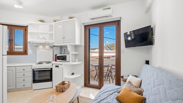 A modern kitchen with white cabinets, a dining table, and a sofa with cushions. - Ageri House | Family Home in Vivlos, Naxos | Sleeps 6 (Vivlos)