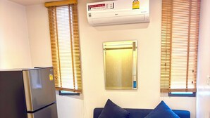 A compact living space with a black refrigerator, a blue sofa, wooden flooring, and an air conditioning unit mounted on the wall. - Adventure Studio Aonang (Krabi)