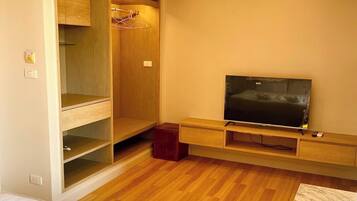 A hotel room with a wooden floor, a TV on a wooden stand, a wardrobe, and a bed with towels.