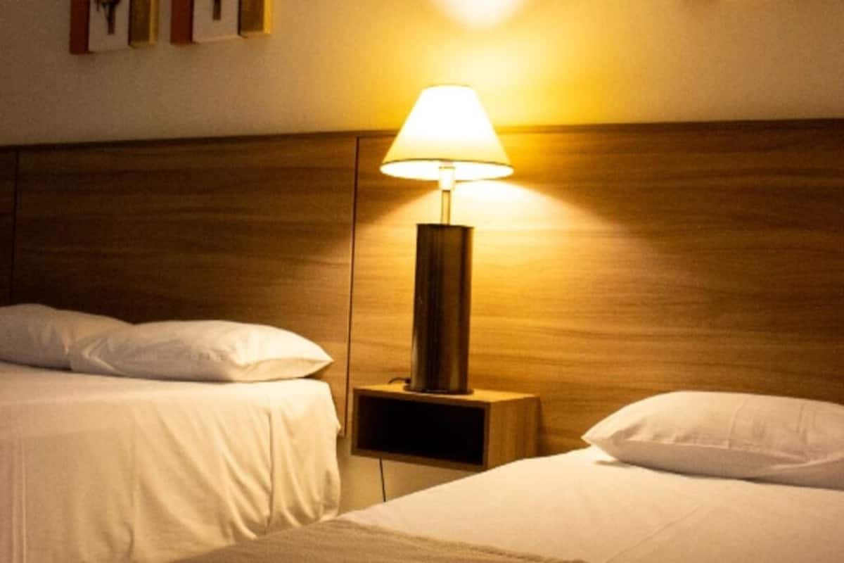 A hotel room with two beds, a nightstand with a lamp, and a wooden headboard.