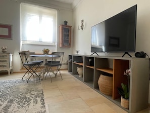 Ein Wohnzimmer mit Fernseher, Esstisch, Stühlen, einer Kommode und einem Fenster.