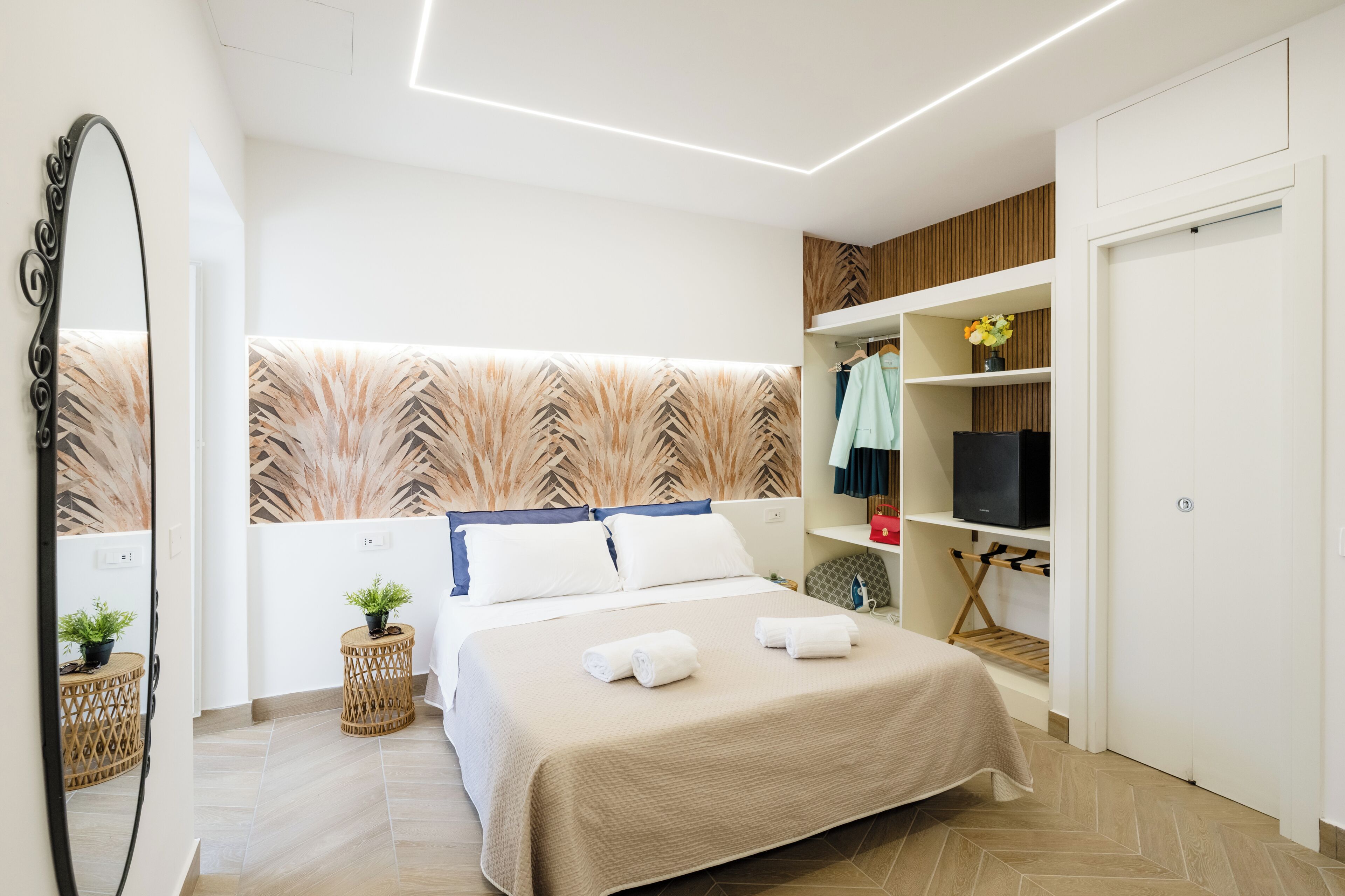 A modern hotel room with a bed, a TV, a wardrobe, and a mirror.