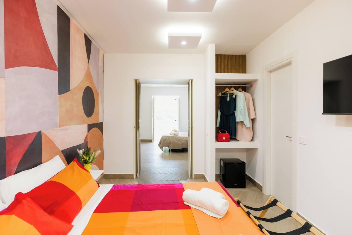 A hotel room with a bed, a wardrobe, a television, and a hallway leading to another room.