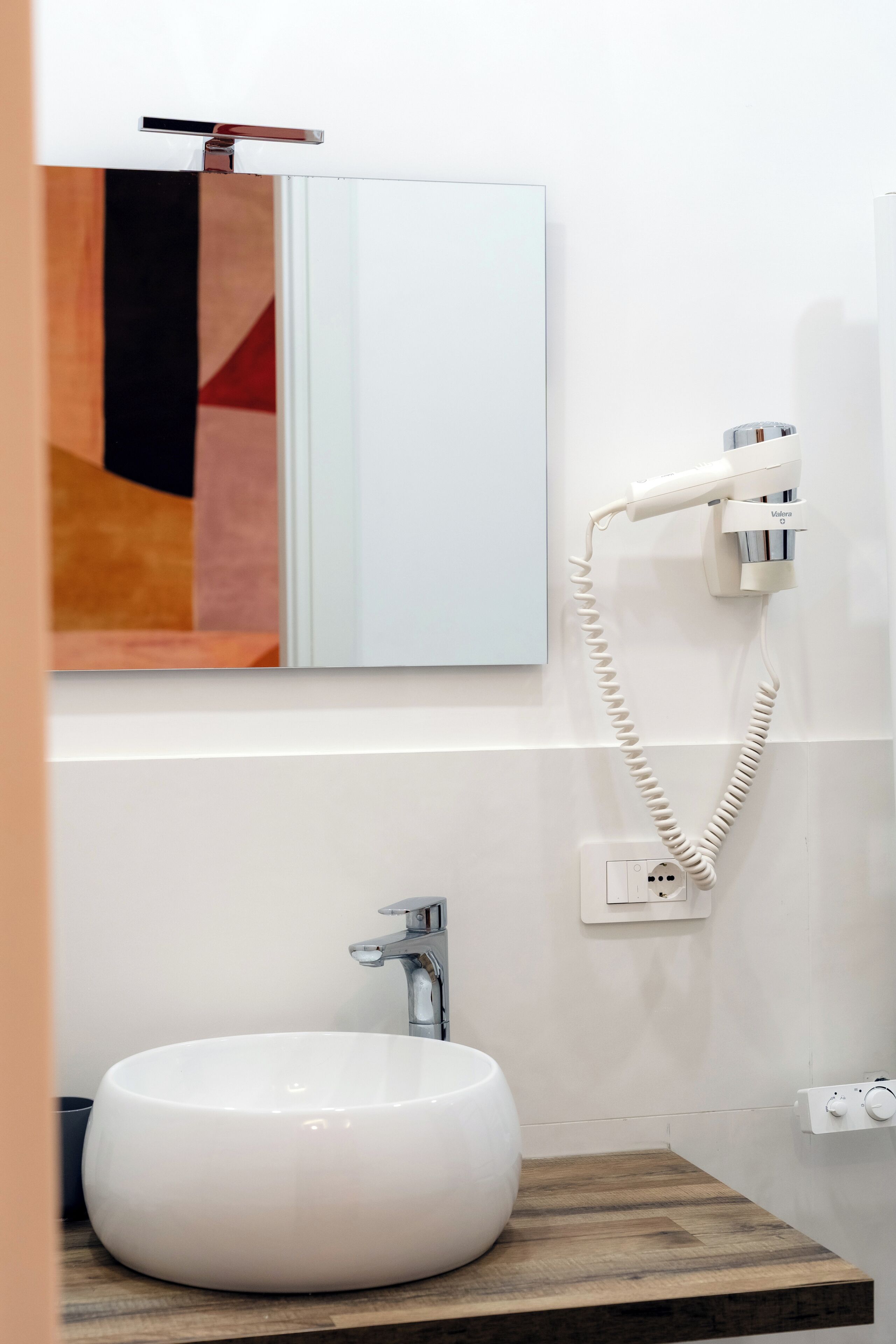 Een badkamer met een wit wastafelmeubel, een spiegel, een handdoekrek en een föhn aan de muur.