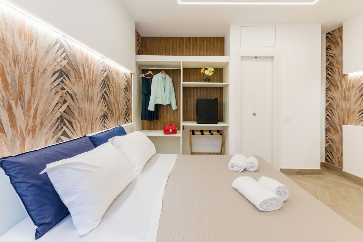 A hotel room with a bed, a wardrobe, a TV, and a small table with towels.