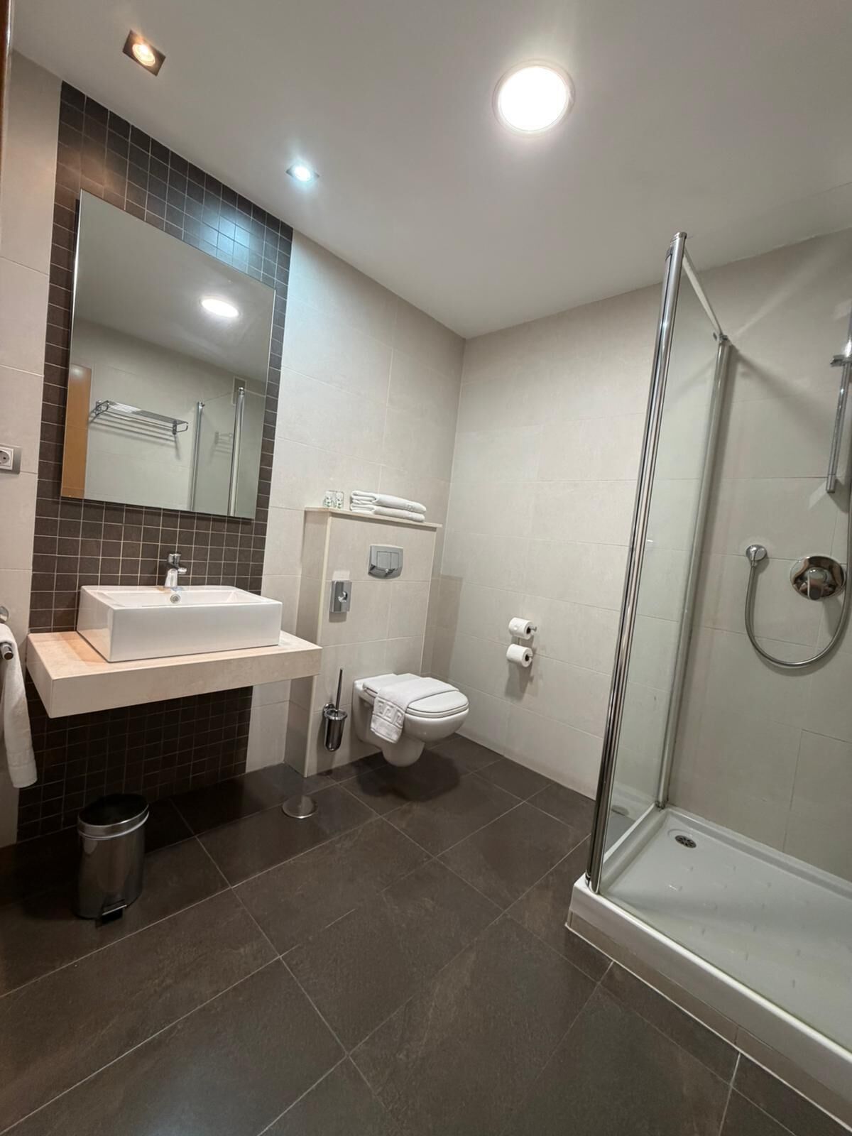 Un baño moderno con ducha de vidrio, lavamanos blanco y retrete.