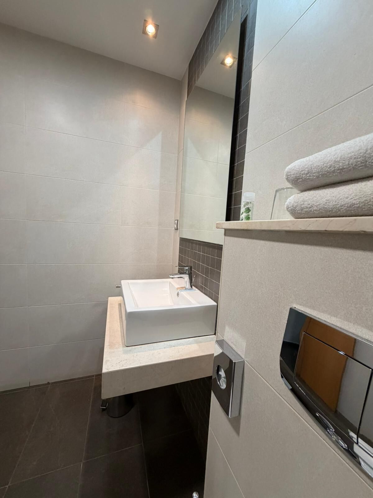 Une salle de bain moderne avec un lavabo blanc, des carreaux de sol foncés, un miroir et un porte-serviettes.