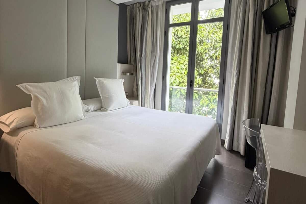 A modern bedroom with a large bed, a flat-screen TV, and a window with curtains.