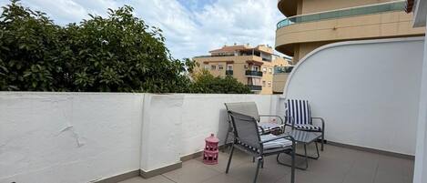 En takterrass med en vit vägg, två stolar, ett litet bord och en rosa lykta.