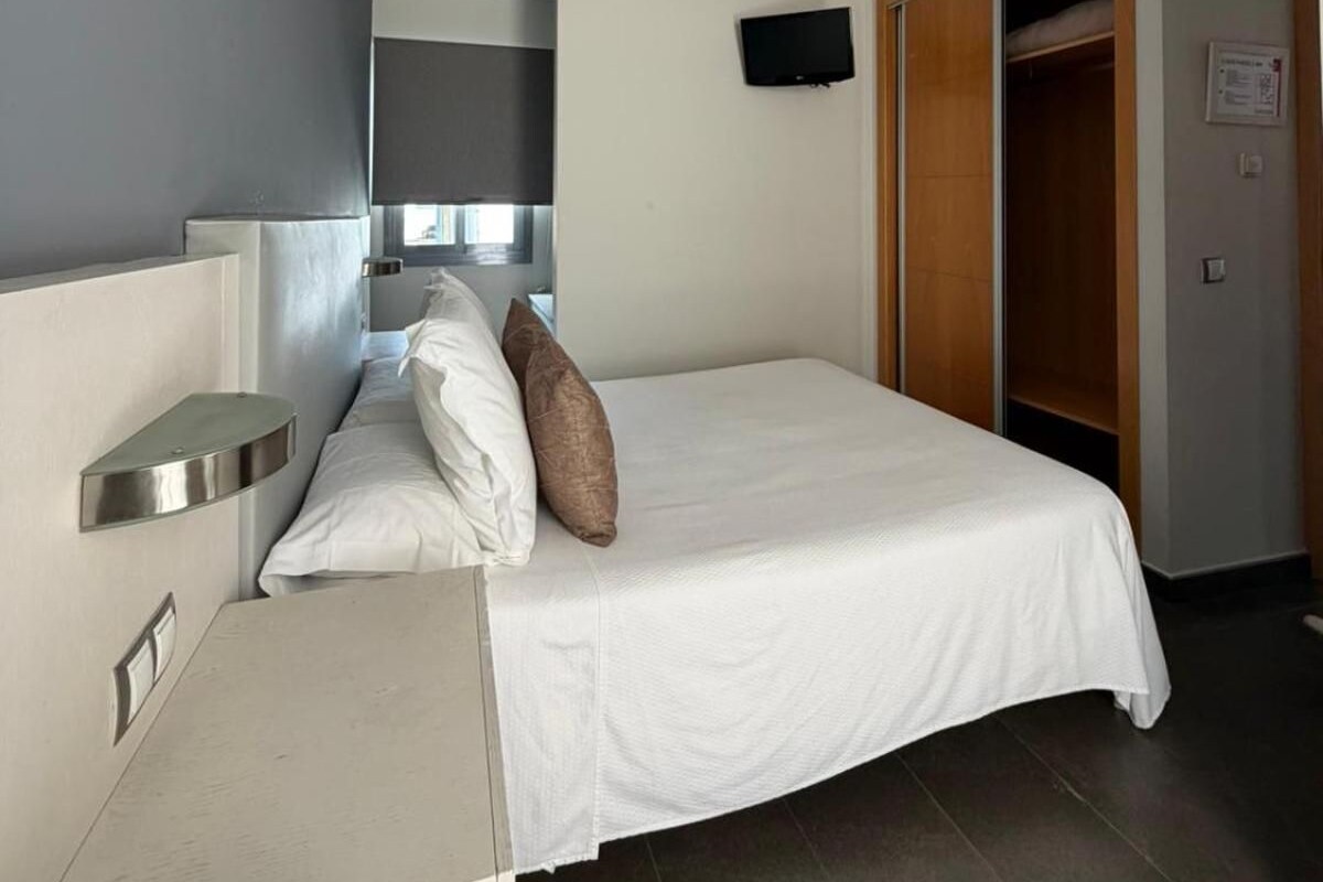 A hotel room with a bed, bedside tables, a TV, and a wardrobe.