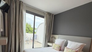 Une chambre d’hôtel dotée d’un grand lit, d’un téléviseur fixé au mur et d’une porte-fenêtre coulissante donnant sur un espace extérieur.
