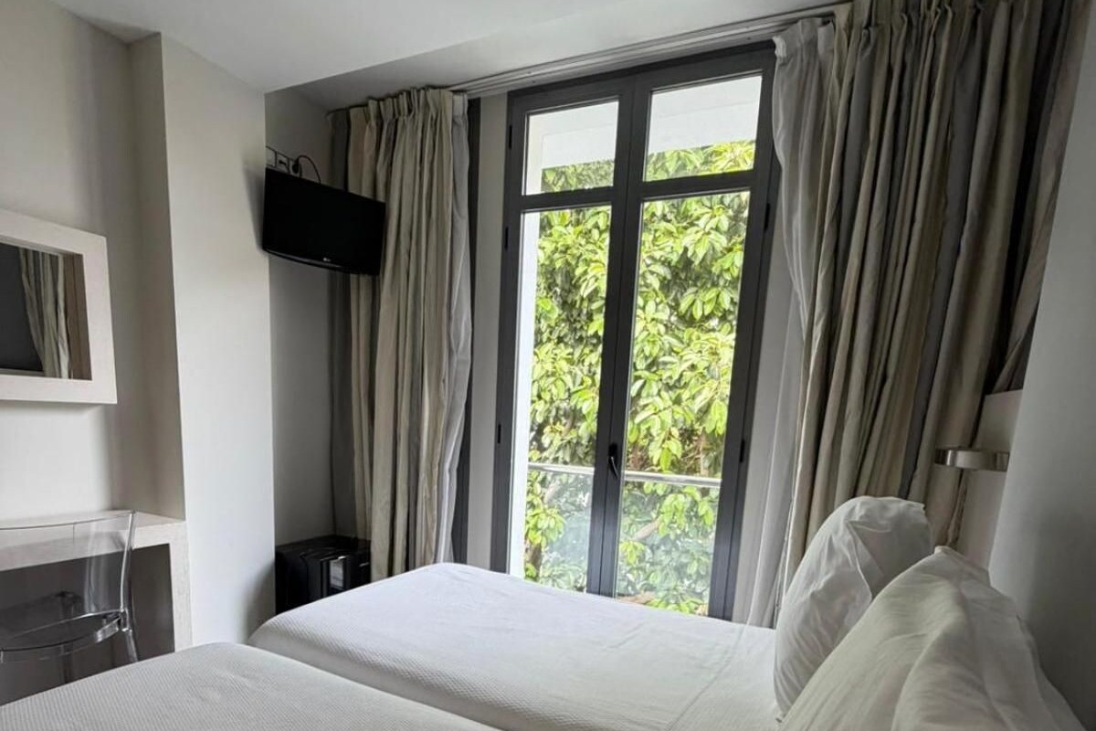 A hotel room with two beds, a desk, a TV, and a window with curtains.