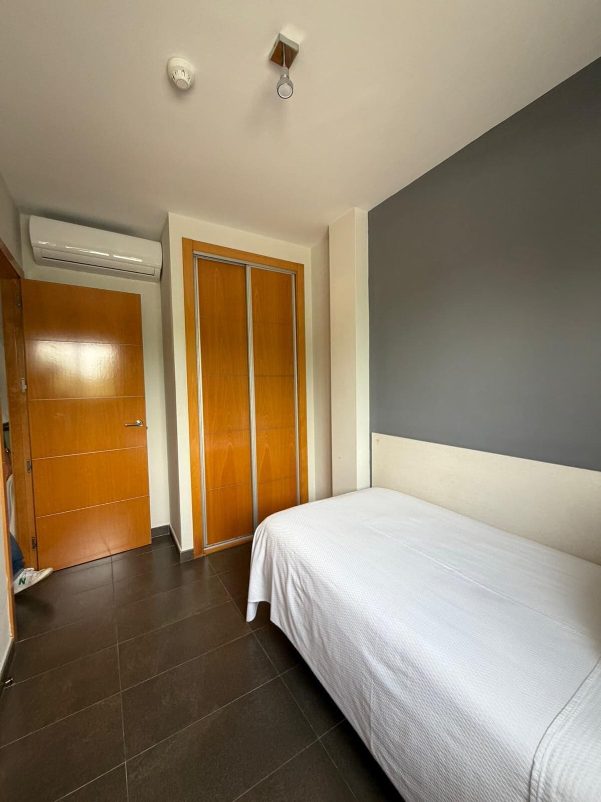 Un dormitorio con cama, armario, puerta y aire acondicionado.