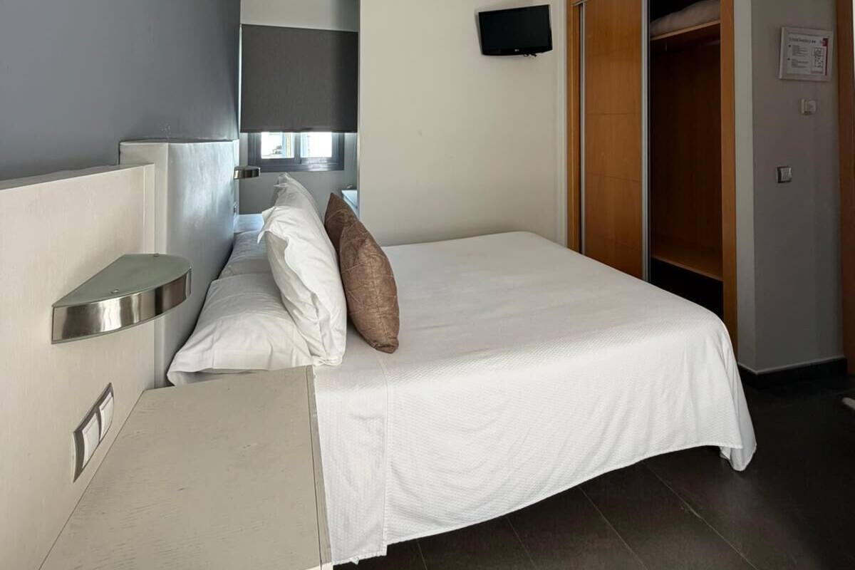 A modern hotel room with a bed, bedside table, and a TV mounted on the wall.