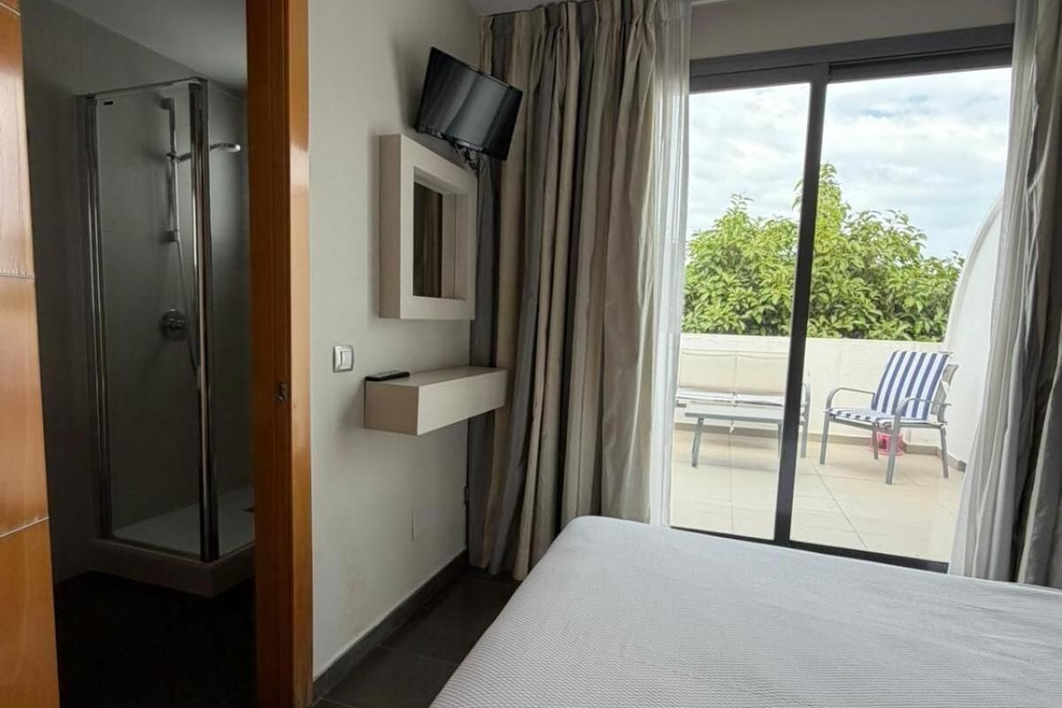 A hotel room with a bed, a television mounted on the wall, a shower, and a view of the outdoors.