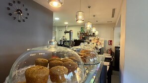 Une vitrine de boulangerie présentant des pâtisseries sous des cloches de verre, une horloge au mur et des lampes suspendues.