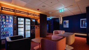 A modern lounge area with vending machines labeled 'Snacks,' 'Breakfast,' 'Water,' and 'Coffee.' There are comfortable seating areas and a wall-mounted sign with 'Espresso' and 'Miss Rouge.' - Yuko Residence (Jasło)