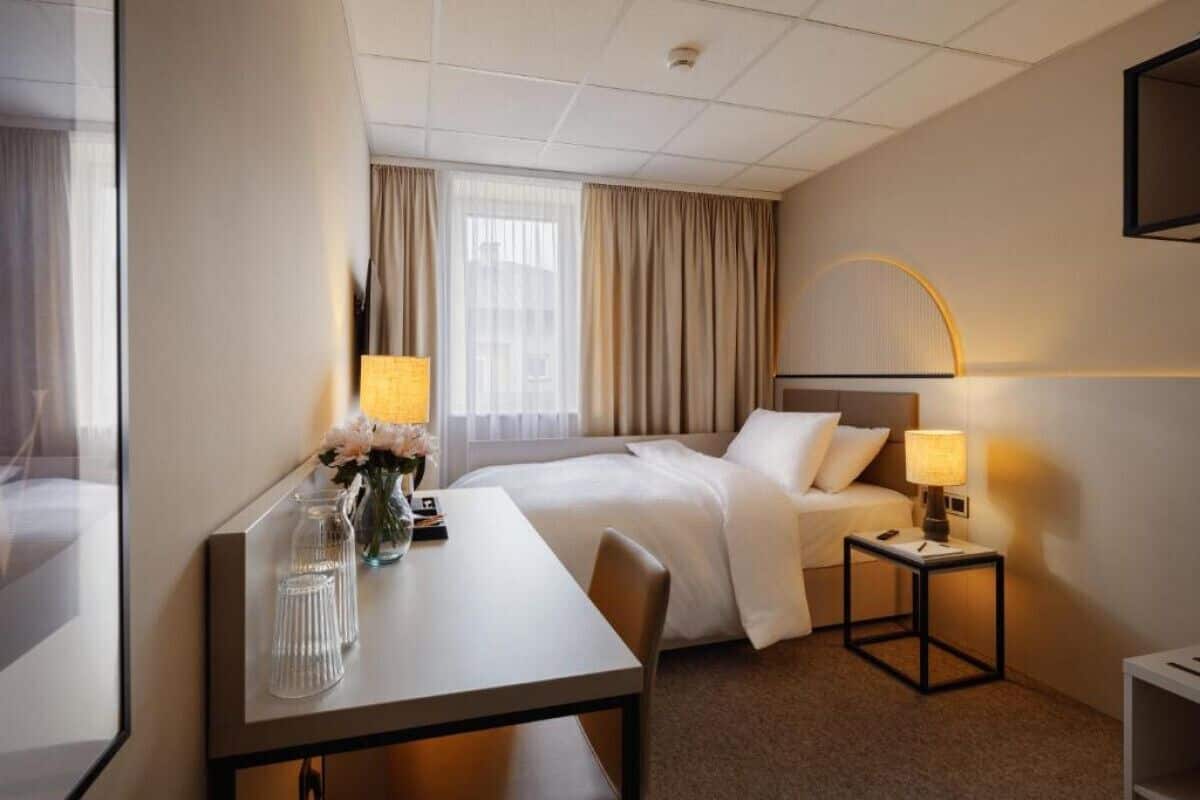 A hotel room with a bed, bedside tables, a desk, and a mirror.