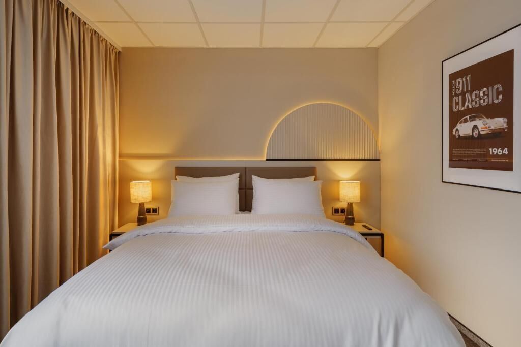 Une chambre d’hôtel avec un grand lit, deux lampes de chevet, une tête de lit au motif circulaire et une affiche accrochée au mur.