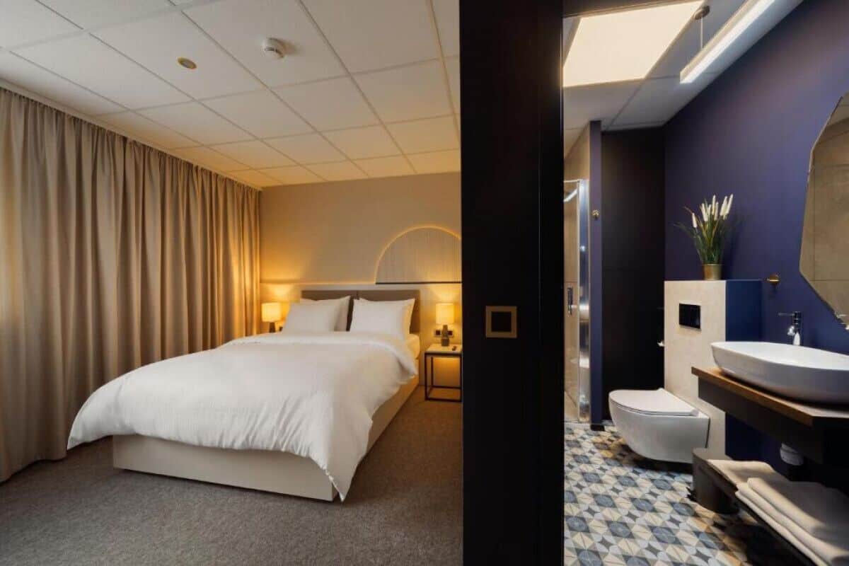 A hotel room with a bed, a nightstand, a lamp, a bathroom with a sink and toilet.