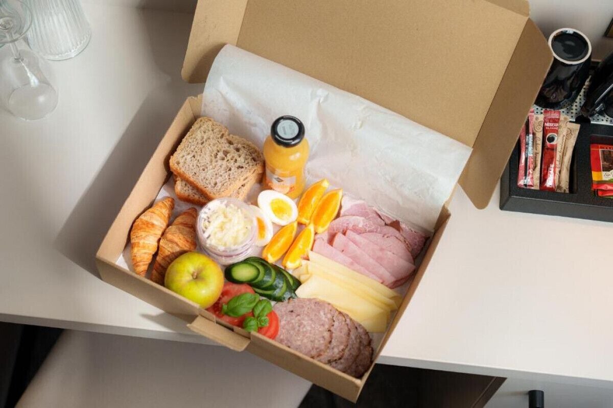 En låda med ett urval av olika livsmedel, inklusive bröd, ost, skinka, ägg och frukt.