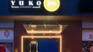A hotel entrance with a neon sign, a blue door, and potted plants. - Yuko Residence (Jasło)