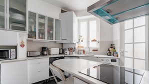 Een moderne keuken met witte kasten, een inbouwoven, een magnetron en een glazen eettafel.