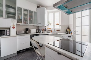 Eine moderne Küche mit weißen Schränken, einem Einbauofen, einer Mikrowelle und einem Esstisch aus Glas.