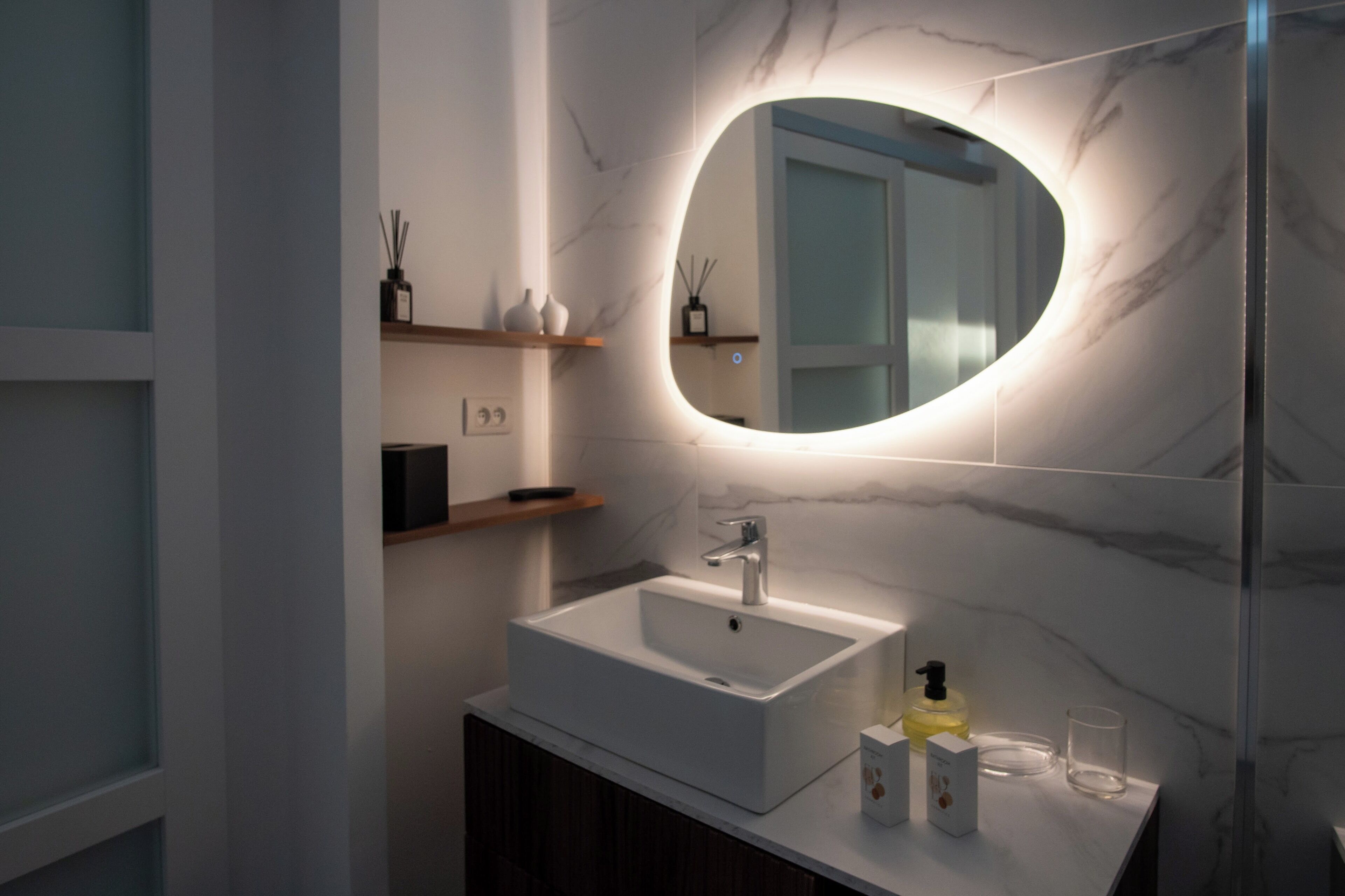 Une salle de bain moderne avec un lavabo blanc, un miroir à cadre ovale et un mur en marbre.