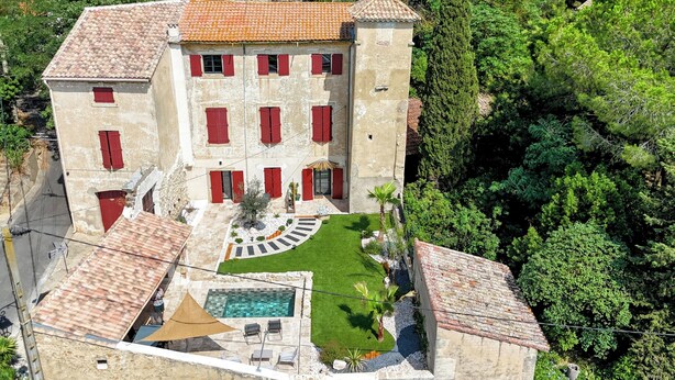 A large building with multiple red shutters, a swimming pool, and a well-maintained garden.