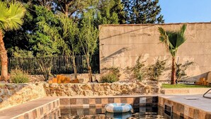 A swimming pool with checkered tiles, surrounded by a stone wall and trees.
