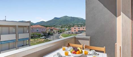A balcony with a table set for breakfast, a bowl of fruit, and glasses of orange juice.