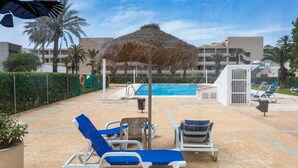 A pool area with lounge chairs, a thatched umbrella, and a building in the background. - Charming Bungalow With Ocean Views in Roquetas de Mar (Roquetas de Mar)